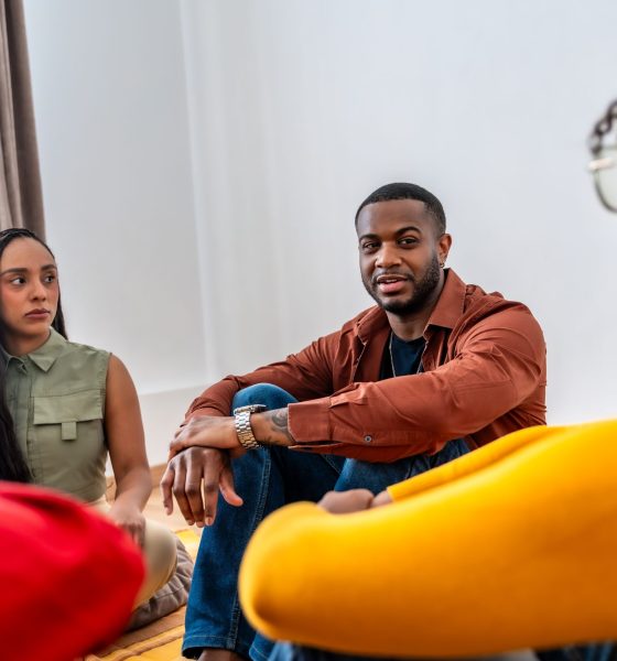 Diverse individuals sitting on the floor, actively listening and engaging in a therapy or support group session, sharing experiences and offering mutual encouragement