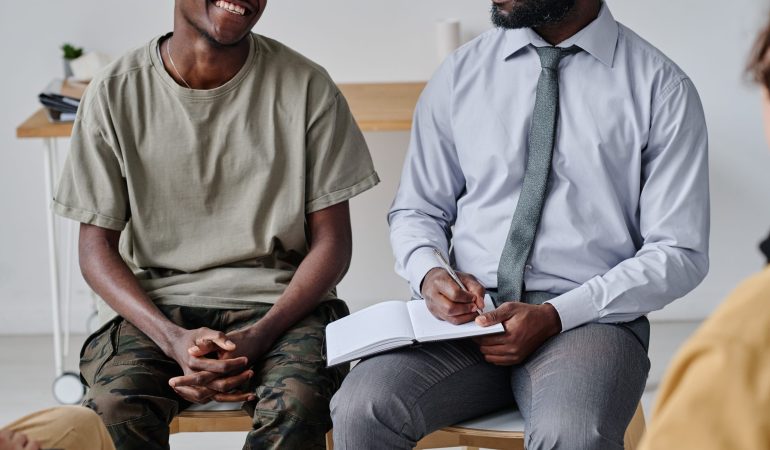 African psychiatrist talking to patient and making notes in notepad at psychology class