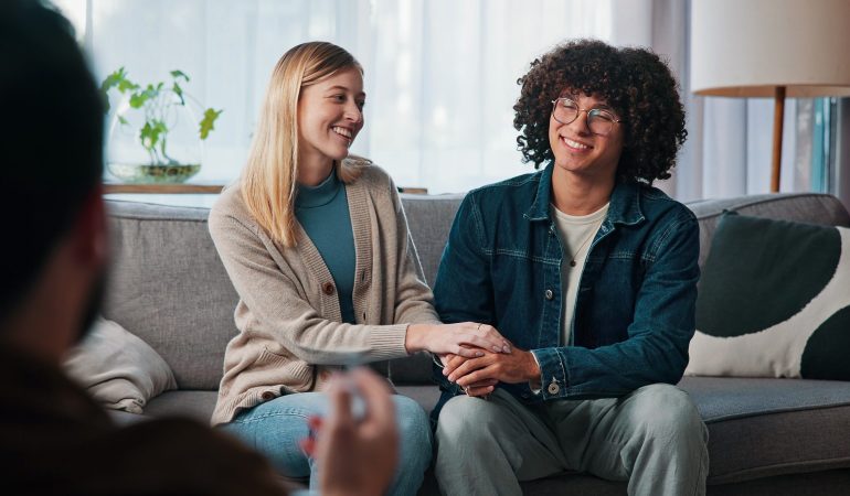 Psychologist, happy couple and holding hands in consultation for love, support or reconciliation. Man, woman and counseling with therapist for advice, save marriage or help in office with solution