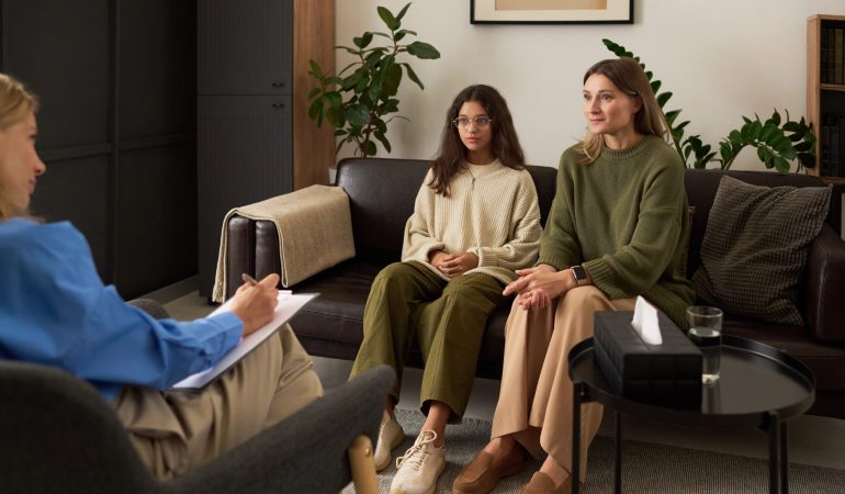 Full length portrait of concerned mother with teenage girl talking to female therapist during family consultation, copy space