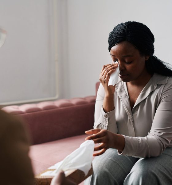 Young stressed female patient taking paper handkerchief to wipe tears while describing her problems to psychoanalyst at session